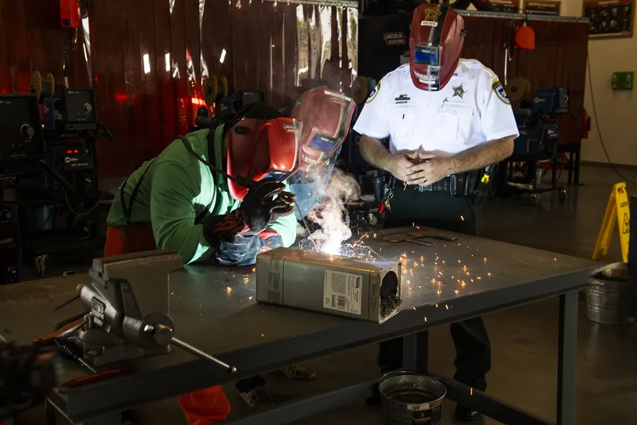 Detention deputy assisting inmates with soldering under supervision