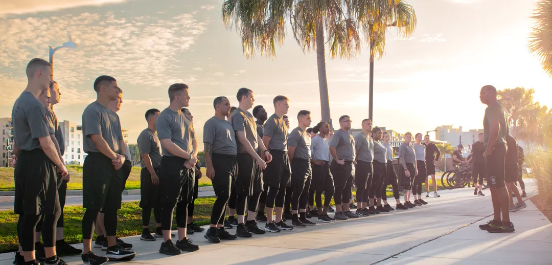 Cadets attentively listening to an instructor during an outdoor physical training session.