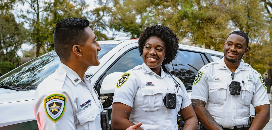 Three law enforcement officers in uniform chatting by patrol car