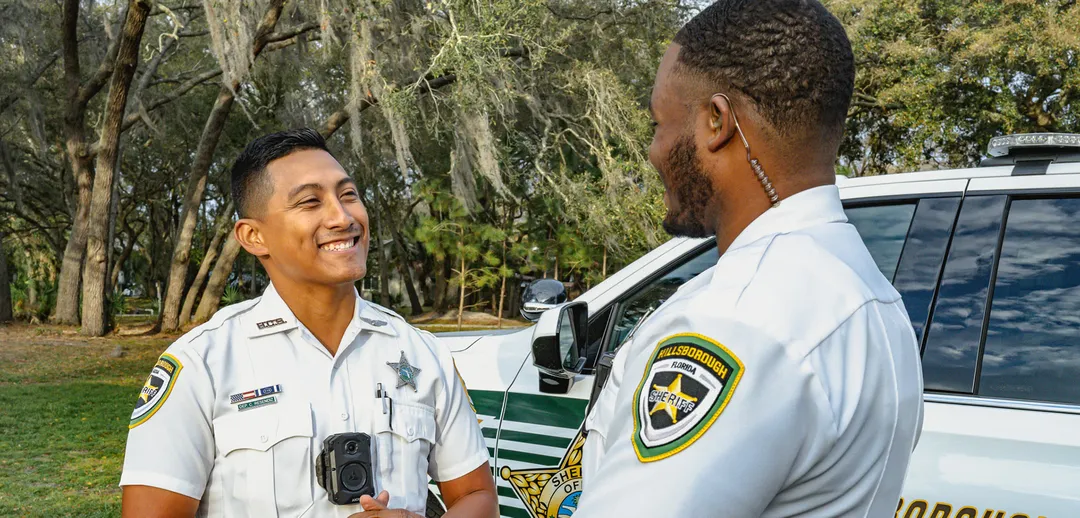 Two smiling patrol deputies in uniform having a discussion outdoors.