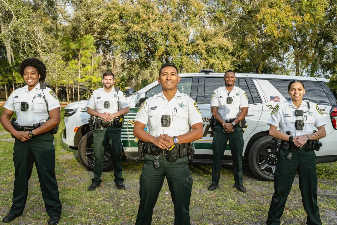 Five deputies in uniform standing proudly in front of patrol vehicle